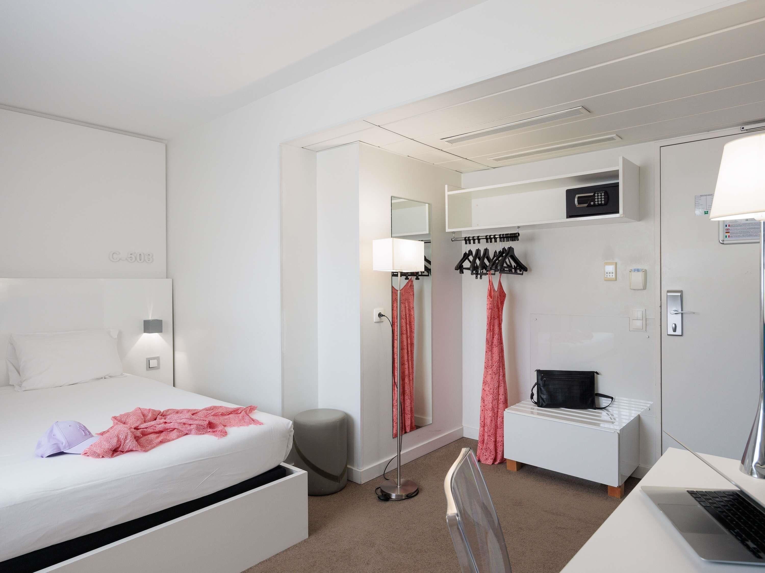 A hotel room with a bed, desk, chair, and a wardrobe.