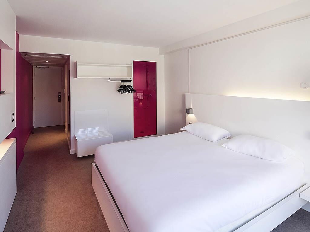Habitación de hotel con una cama grande, una mesita de noche, un armario y un baño con ducha.