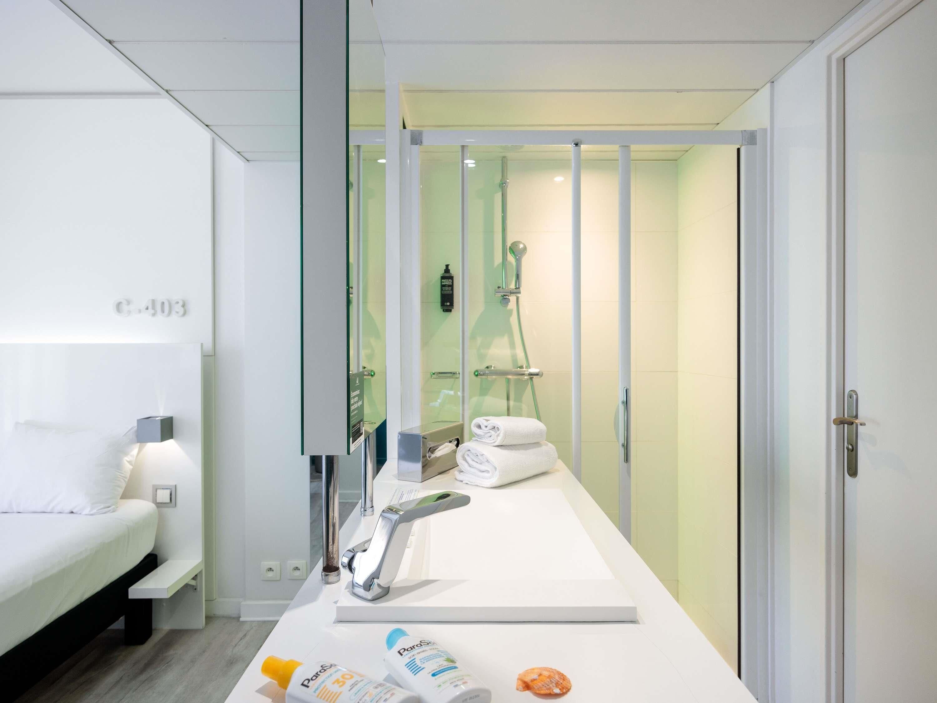 A modern bathroom with a shower, a sink, and a mirror. There is a towel rack with towels and toiletries on the counter.