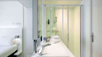 A modern bathroom with a shower, a sink, and a mirror. There is a towel rack with towels and toiletries on the counter.