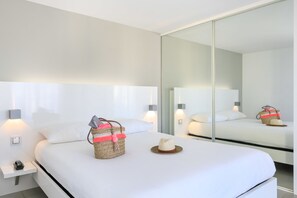 A modern hotel room with a large bed, bedside lamps, a nightstand, a woven bag, and a hat on the bed. - ibis Styles Menton Centre (Menton)