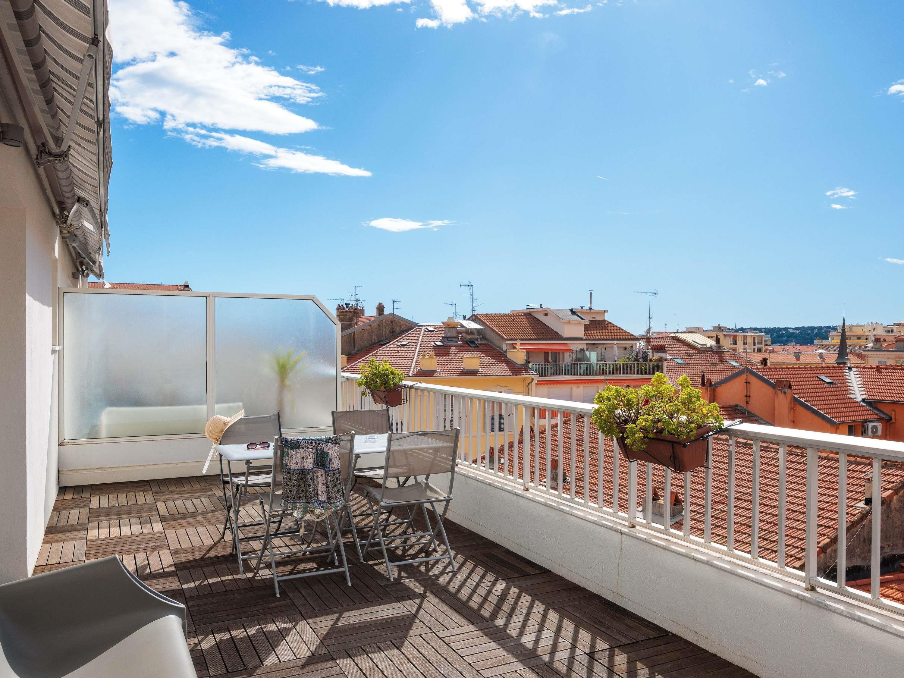 A balcony with a table and chairs, a hanging plant, and a view of the cityscape.