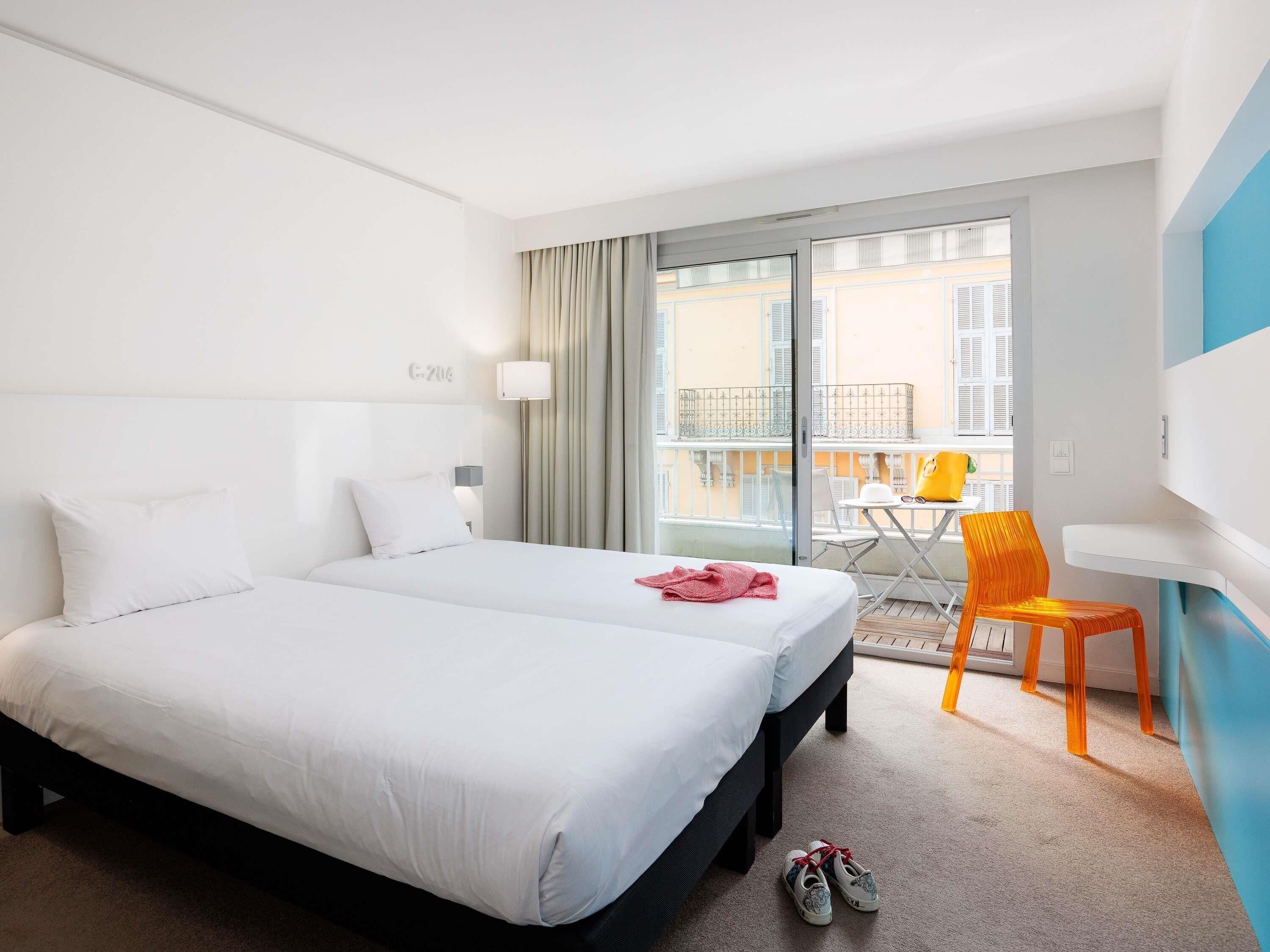 A hotel room with a large bed, a balcony with a table and chairs, and a view of buildings.