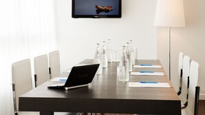 A conference room with a long table, chairs, a laptop, a television, and a lamp. - ibis Styles Menton Centre (Menton)
