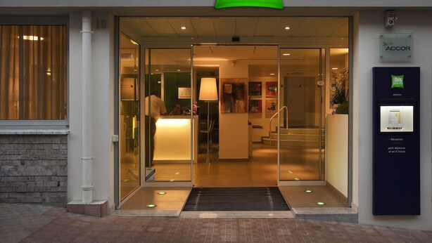 The entrance to an ibis Styles hotel with a reception desk, glass doors, and a digital check-in kiosk. - ibis Styles Menton Centre (Menton)