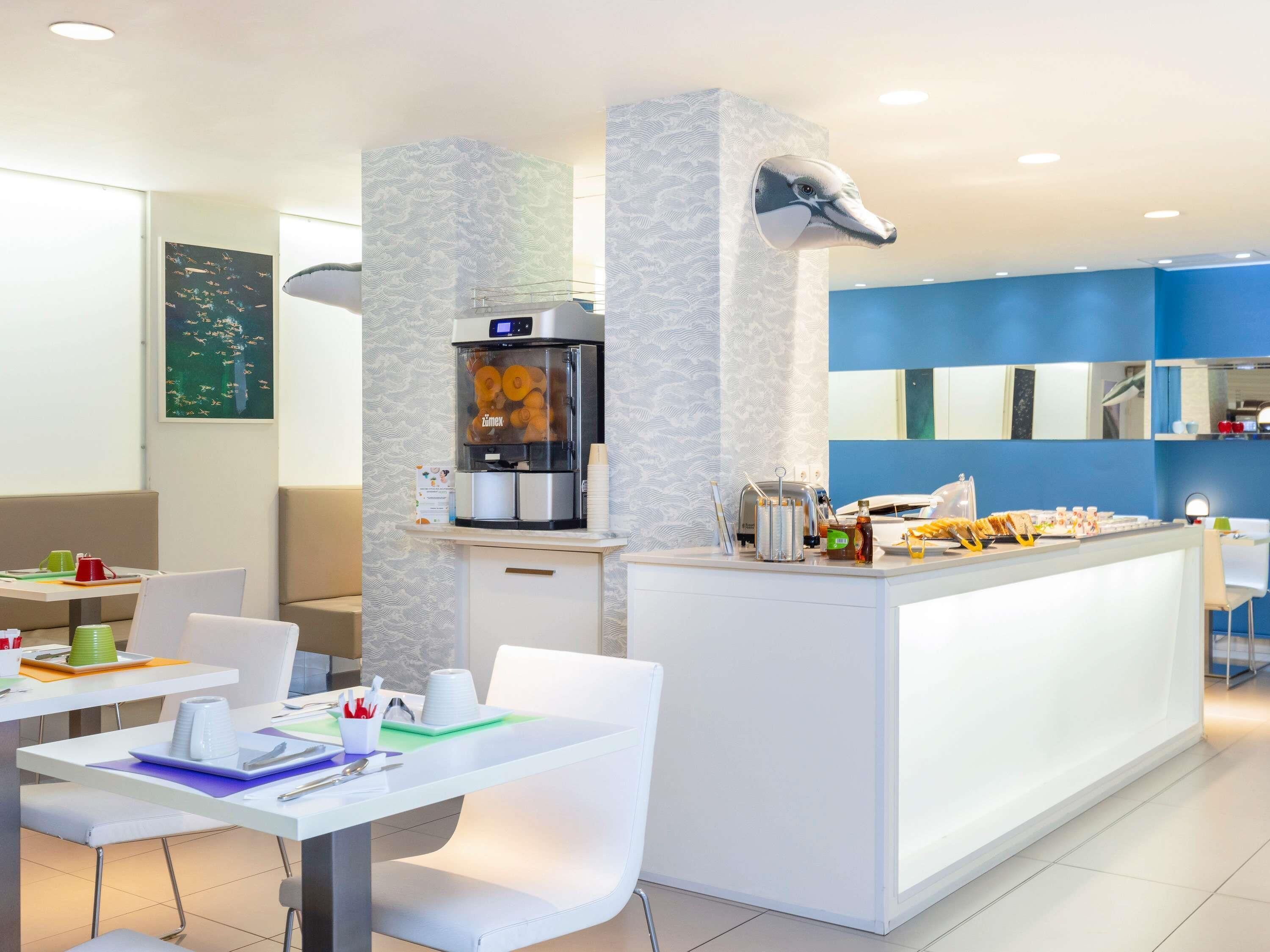 Una habitación de hotel moderna con kitchenette, un área de comedor con mesa y sillas blancas, y un ventanal con vistas.