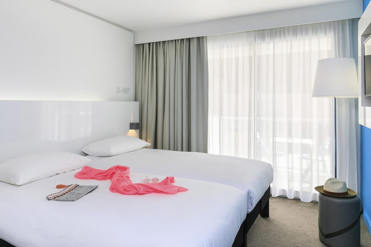 A hotel room with a large bed, a bedside lamp, a window with curtains, and a wall-mounted TV.