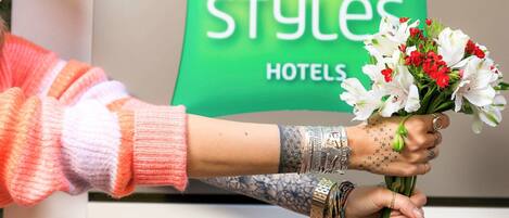Una persona sosteniendo un ramo de flores frente a un letrero que dice 'ibis Styles Hotels'.