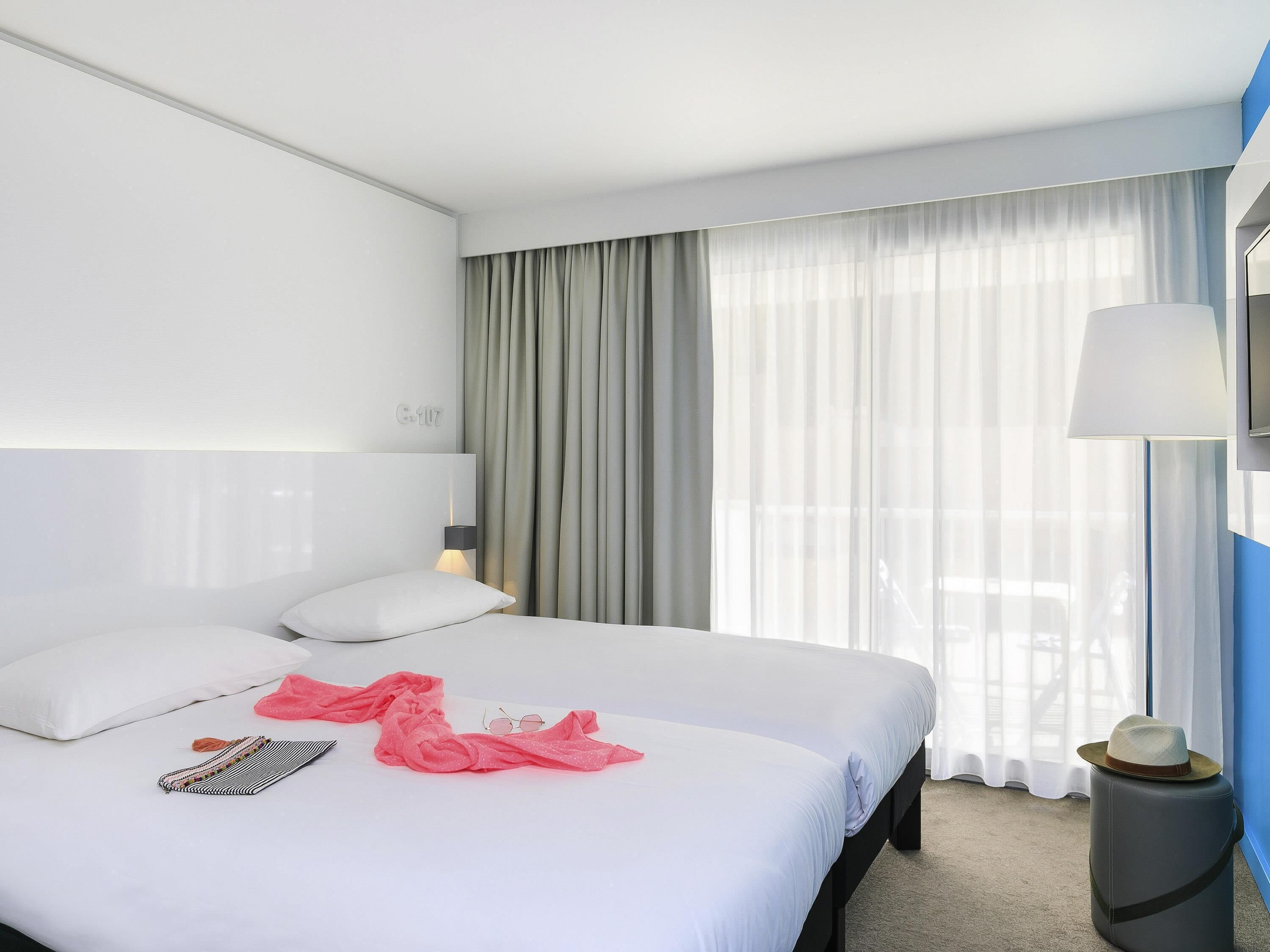 A hotel room with a bed, a nightstand, a lamp, and a window with curtains.