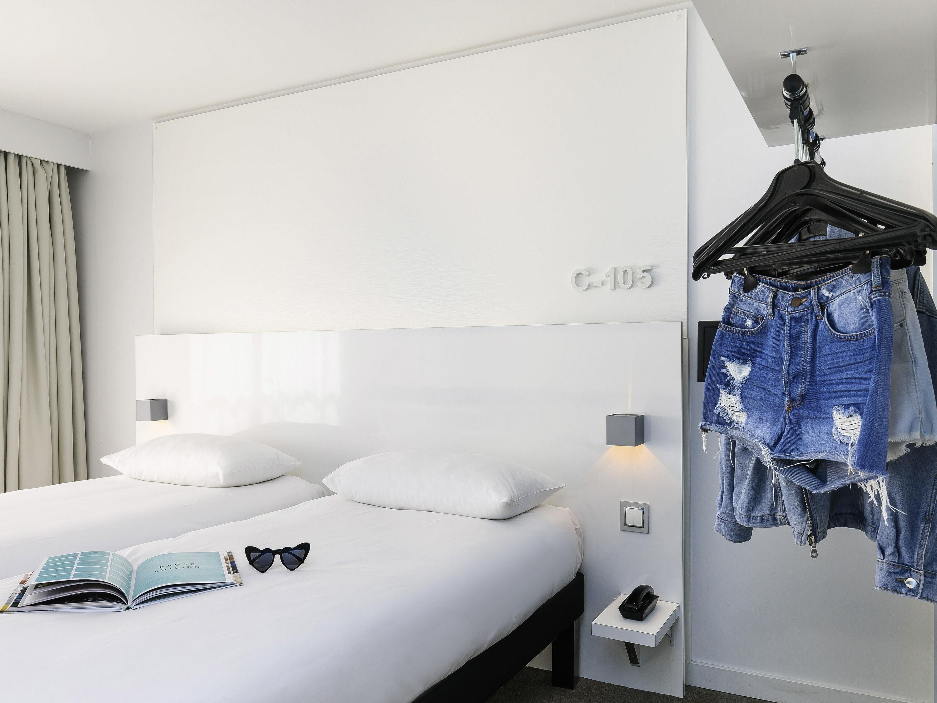 Une chambre d’hôtel moderne avec un grand lit, une table de chevet avec un téléphone et un porte-vêtements.