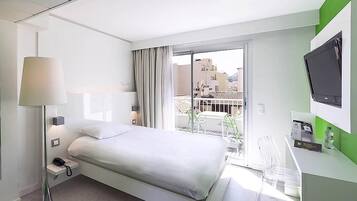 Una habitación de hotel moderna con cama, lámpara de noche y vistas a edificios a través de un ventanal grande.