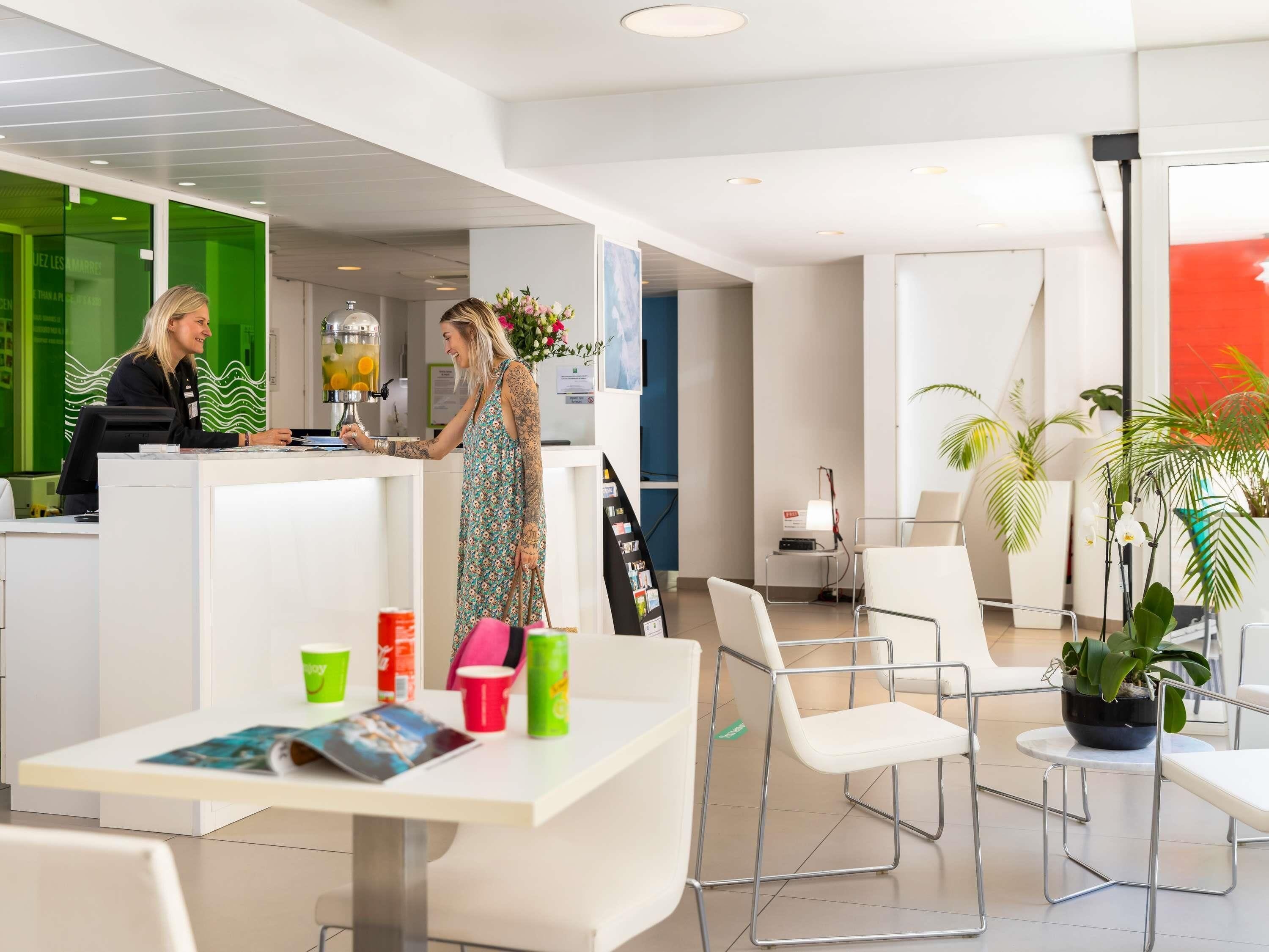 Un hall d’hôtel moderne avec un comptoir d’accueil, un espace salon et des plantes en pot.
