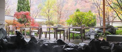 Un jardín japonés tradicional con aguas termales, bancos de madera y vistas al follaje otoñal.