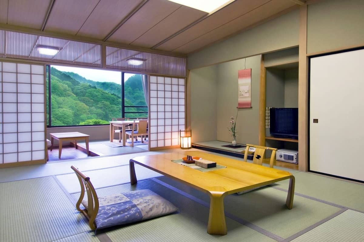 Una habitación tradicional japonesa con suelo de tatami, una mesa baja, un sofá y un televisor.