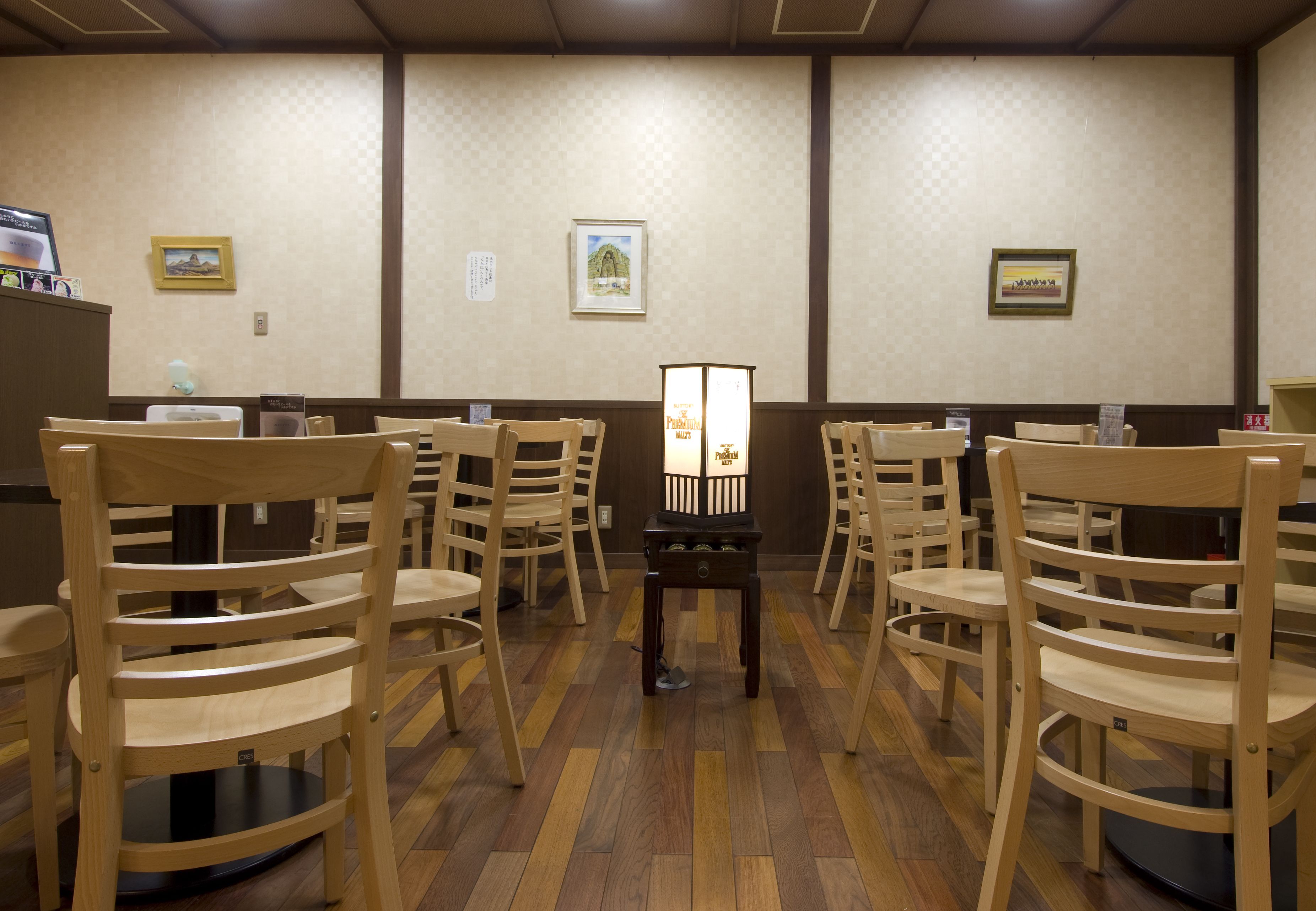 Una habitación con sillas de madera dispuestas en filas, una mesa central y cuadros en las paredes.