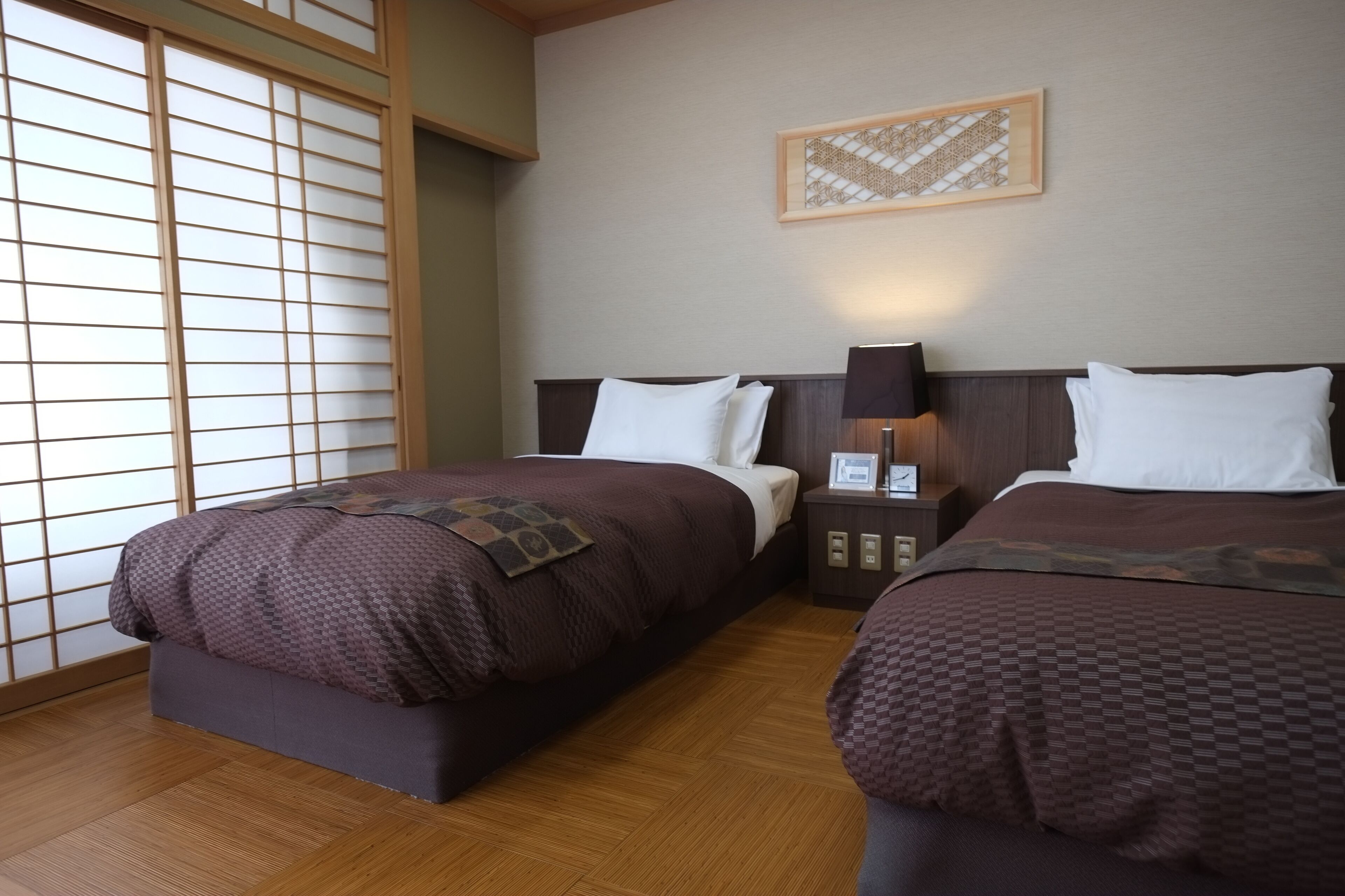 A hotel room with two beds, wooden flooring, a shoji screen, and a framed artwork on the wall.