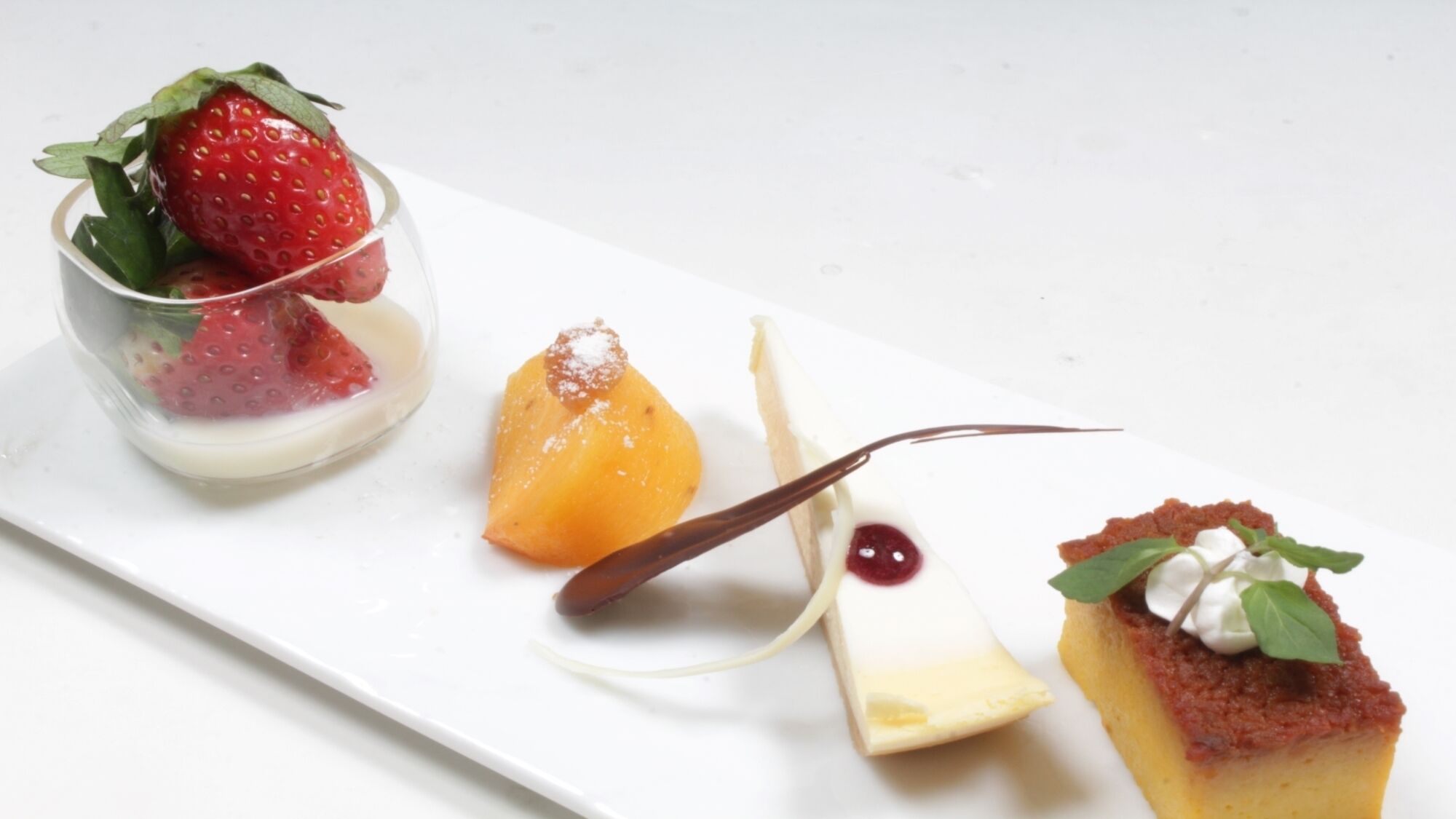 A dessert plate with a strawberry, a peach, a chocolate dessert, and a cheesecake.