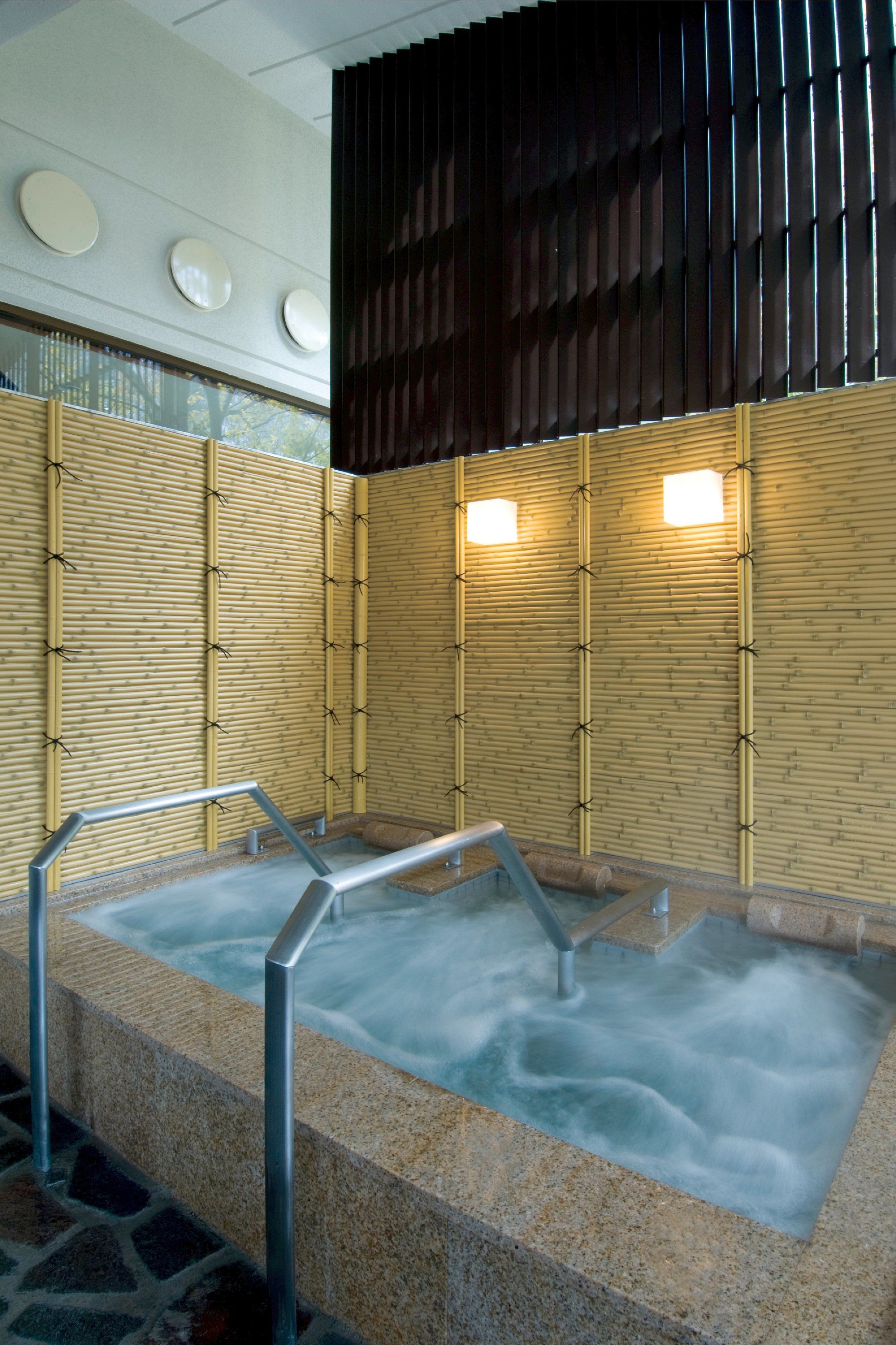 A hot spring area with bamboo walls, metal railings, and a stone floor.