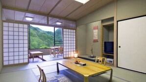 Una habitación japonesa tradicional con suelo de tatami, una mesita baja, sillas, un televisor y vistas a un paisaje verde exuberante.