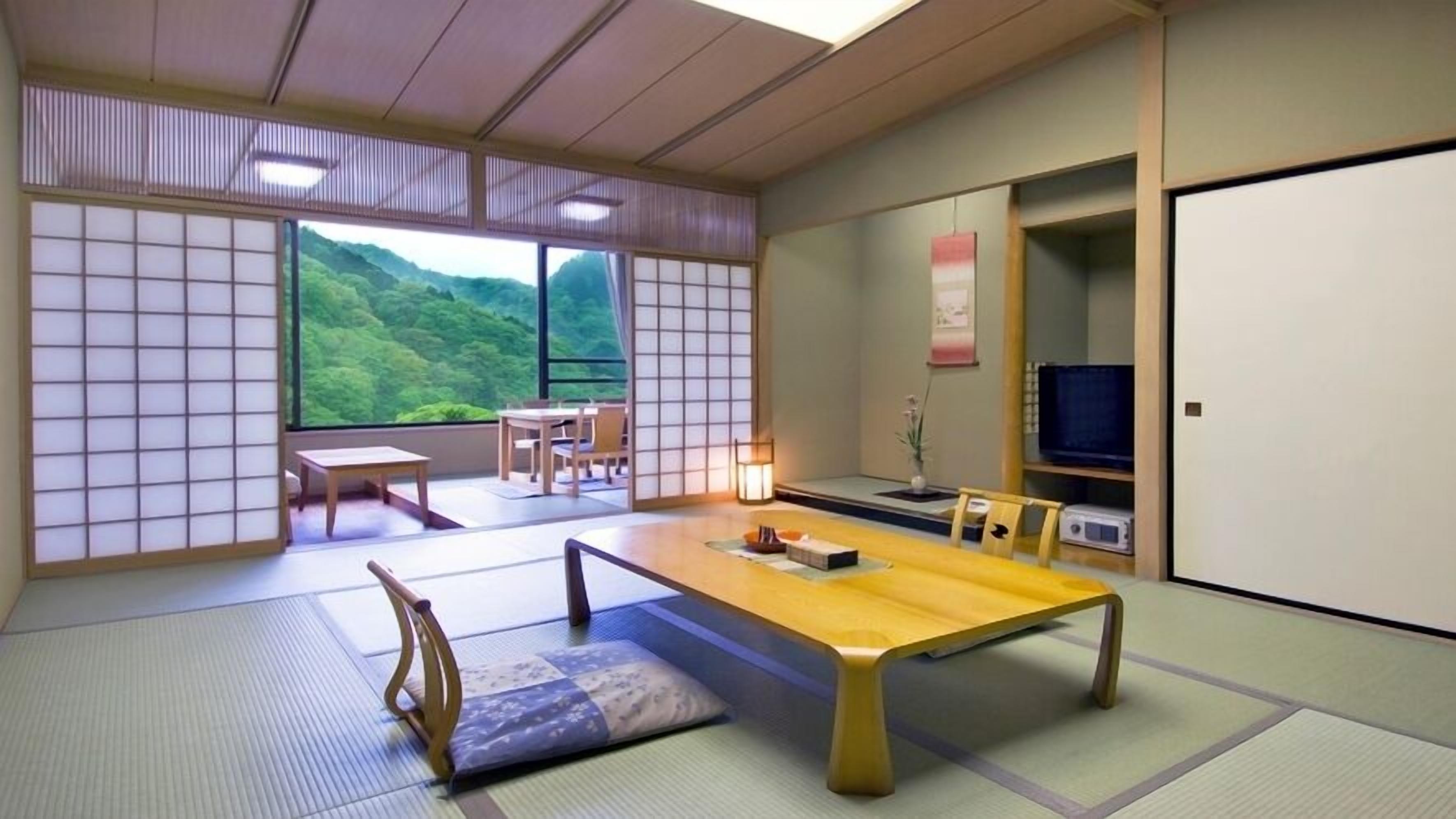 A traditional Japanese room with tatami flooring, a low table, a TV, and a view of a green landscape.