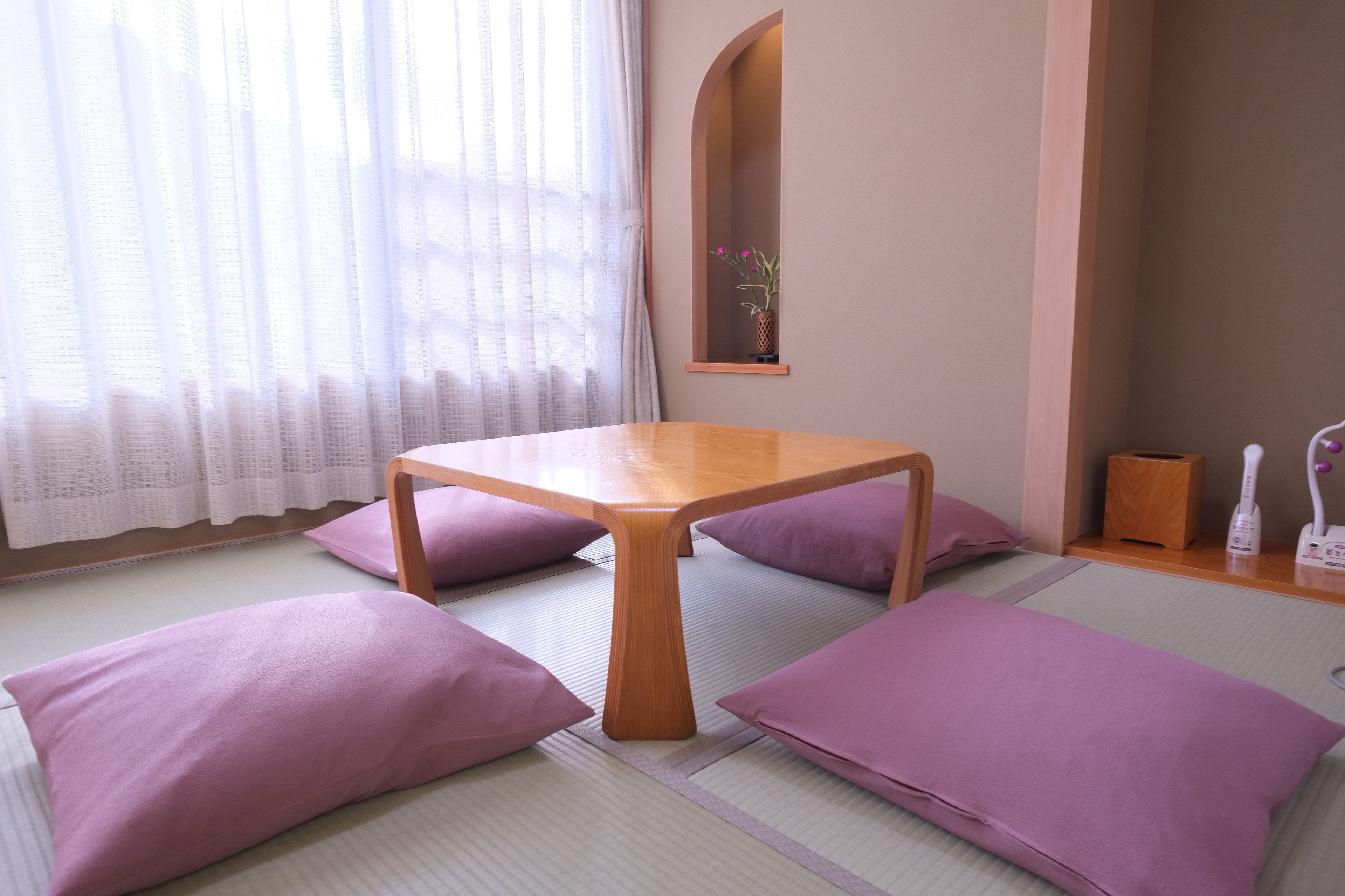 A tatami mat room with a wooden table, purple cushions, and a mirror on the wall.