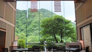 Un restaurante con vistas a una ladera boscosa. Mesas y sillas dispuestas para comer.