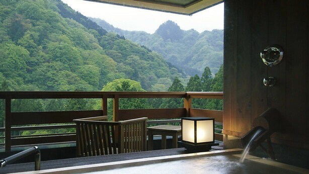 Una terraza de madera con vistas a un exuberante valle verde, una mesa de madera, una silla y un farol encendido.