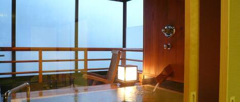A glass-enclosed hot tub with a wooden deck and a chair.