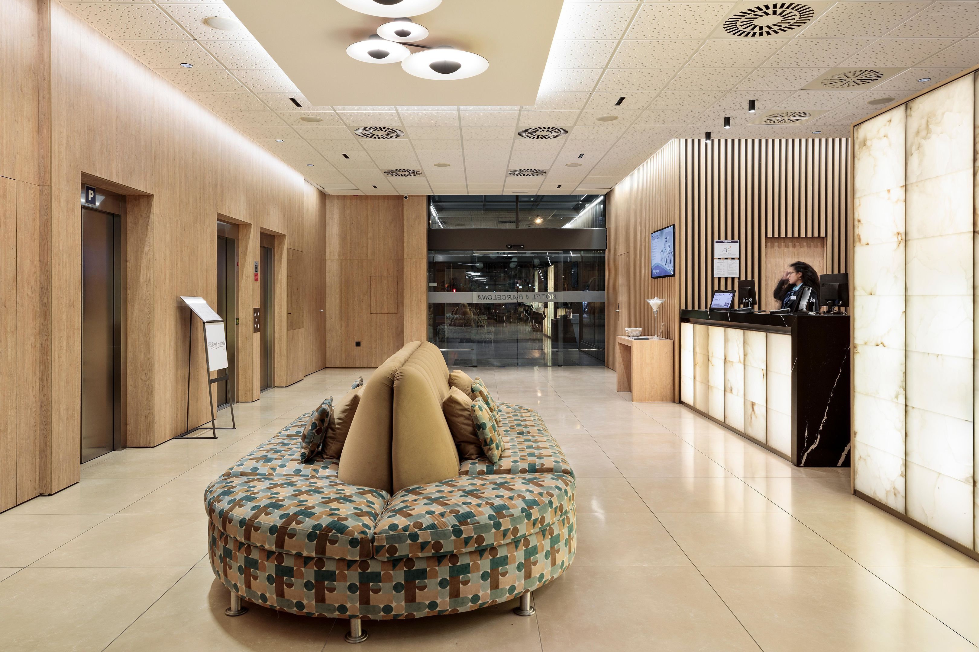 Un hall d’entrée moderne doté d’un espace salon central, d’un comptoir d’accueil et d’un grand écran numérique.