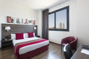 Una camera d'albergo con un letto grande, una scrivania, una sedia, una finestra con vista sulla città e opere d'arte alle pareti.