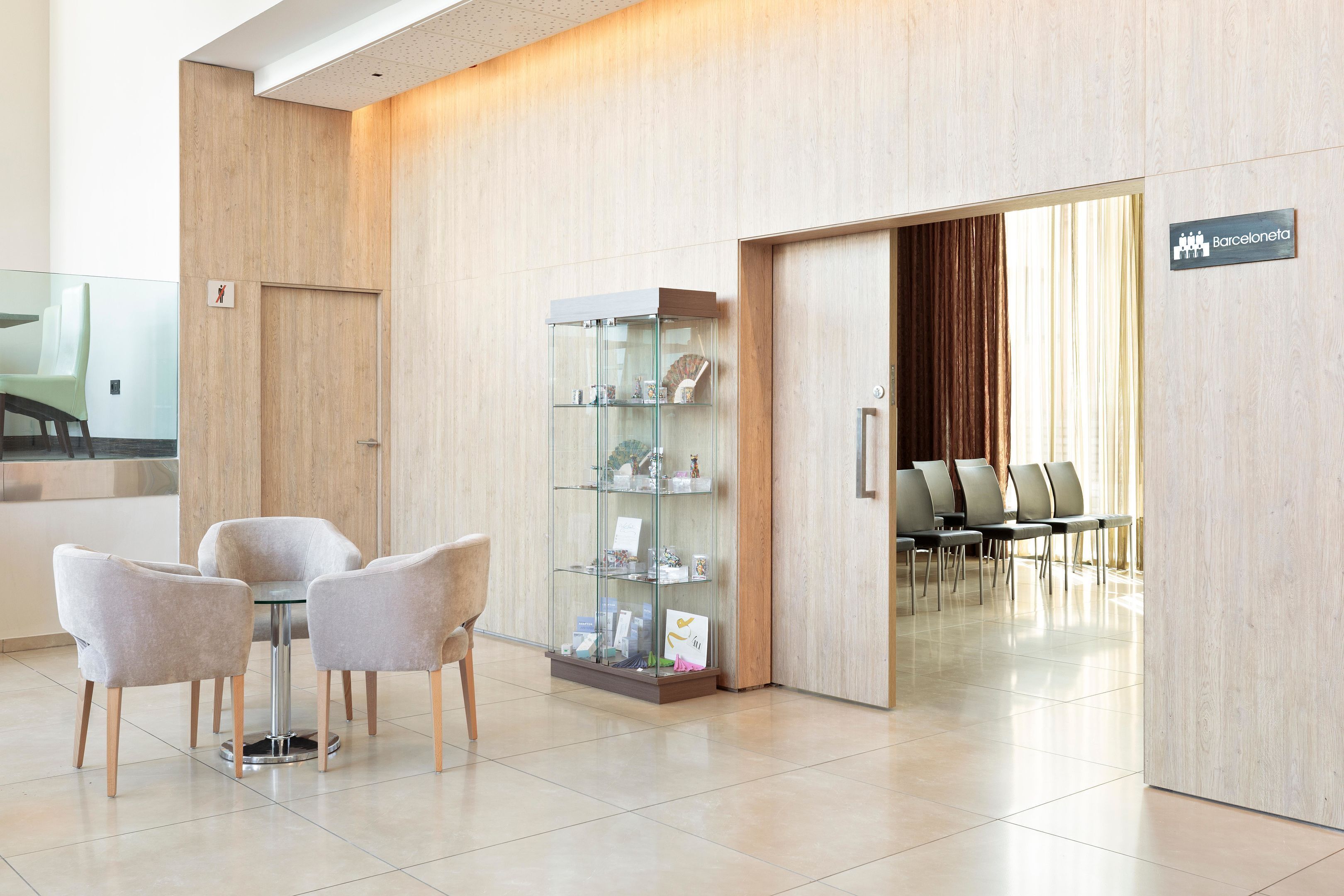 Un espace d’accueil moderne comprenant un présentoir en verre, un coin salon avec des fauteuils et un panneau indiquant que l’on se trouve à « Barcelone ».