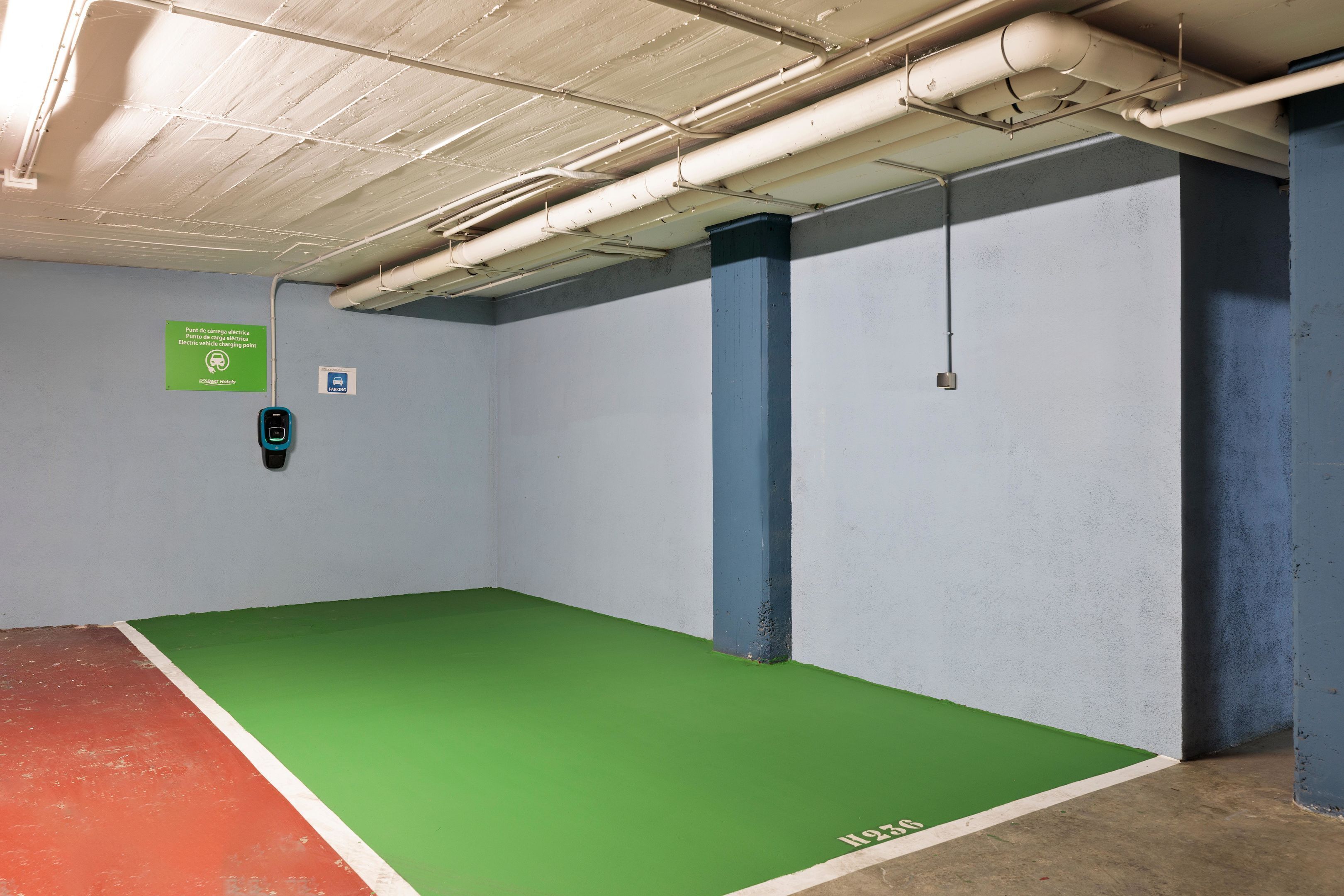 Un garaje para estacionar con pisos pintados de verde y rojo, tuberías de techo blancas y un letrero verde en la pared.
