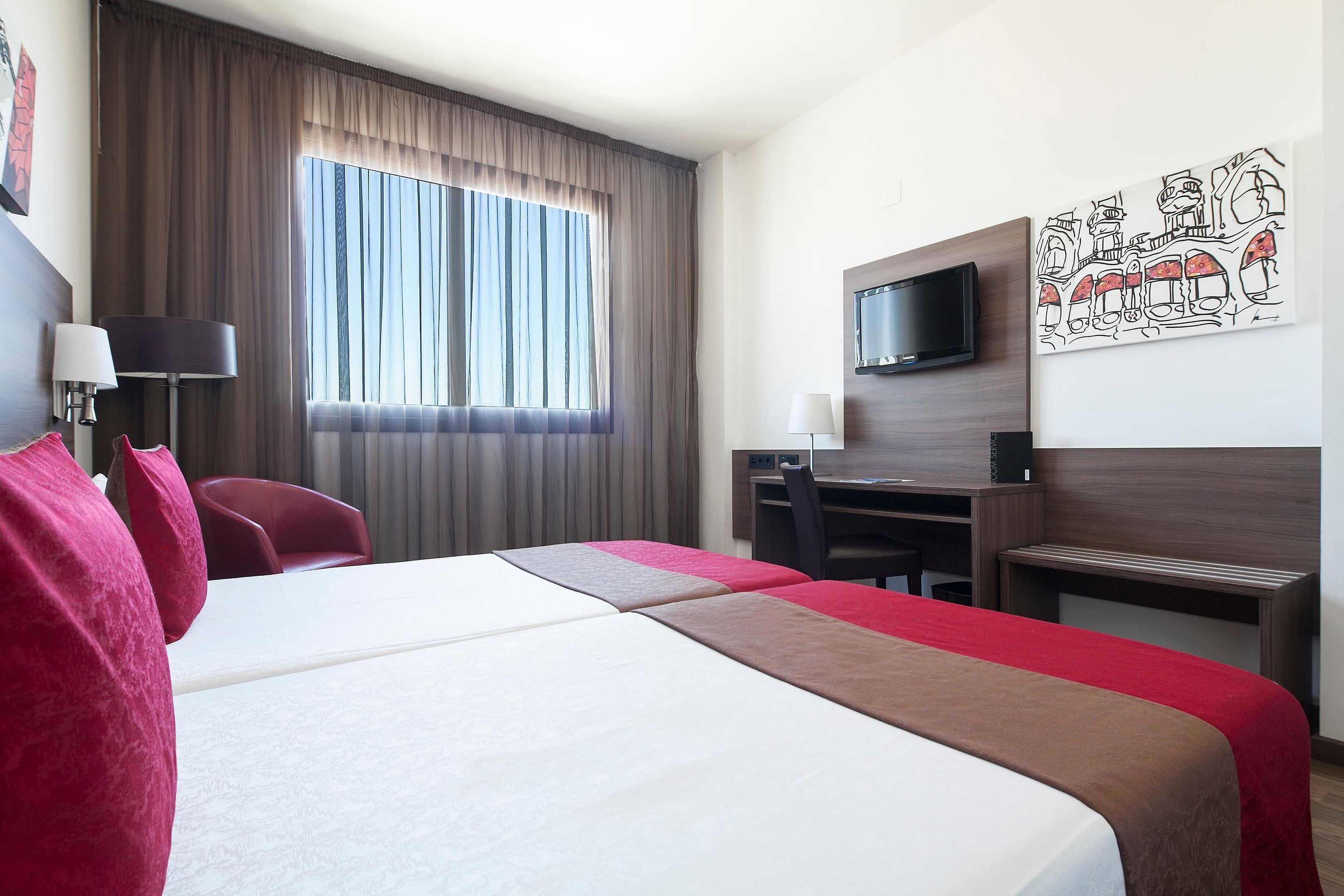 Hotelkamer met een groot bed, een bureau, een stoel, een televisie en een raam met gordijnen.