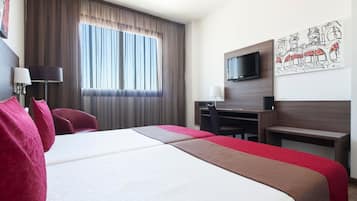 Hotelkamer met een groot bed, een bureau, een stoel, een televisie en een raam met gordijnen.