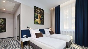 Quarto de hotel com duas camas, uma janela grande com cortinas, um quadro na parede e um tapete estampado.
