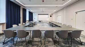 Uma sala de conferência com uma mesa comprida, várias cadeiras e piso coberto por carpete.