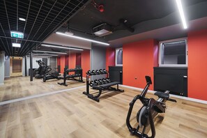 Un gimnasio con equipo de ejercicio, piso de madera y paredes rojas.