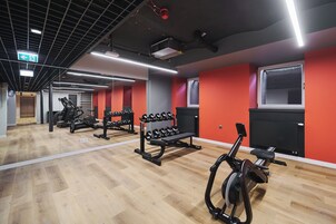 Un gimnasio con equipo de ejercicio, piso de madera y paredes rojas.