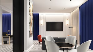 Uma sala de estar moderna com um sofá preto, cadeiras brancas, uma mesa de centro redonda e uma grande TV de tela plana fixada na parede.