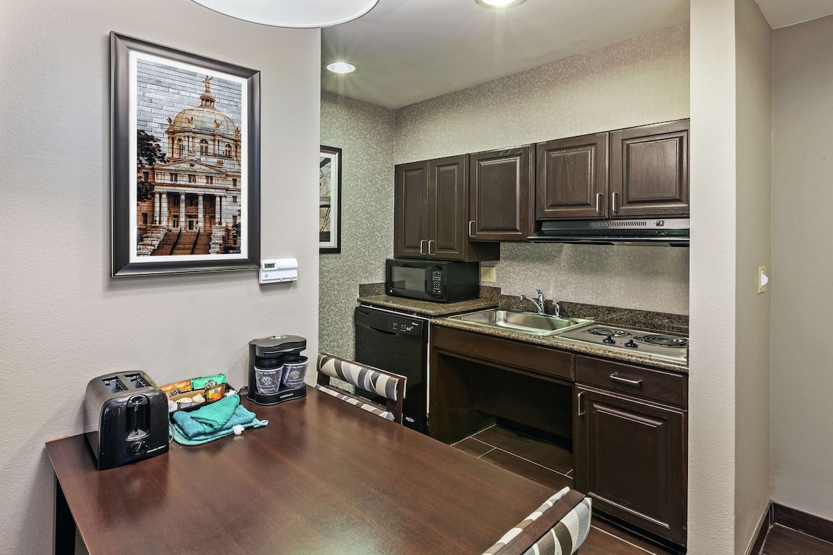 A compact kitchen with dark wooden cabinets, a built-in microwave, and a stainless steel sink.
