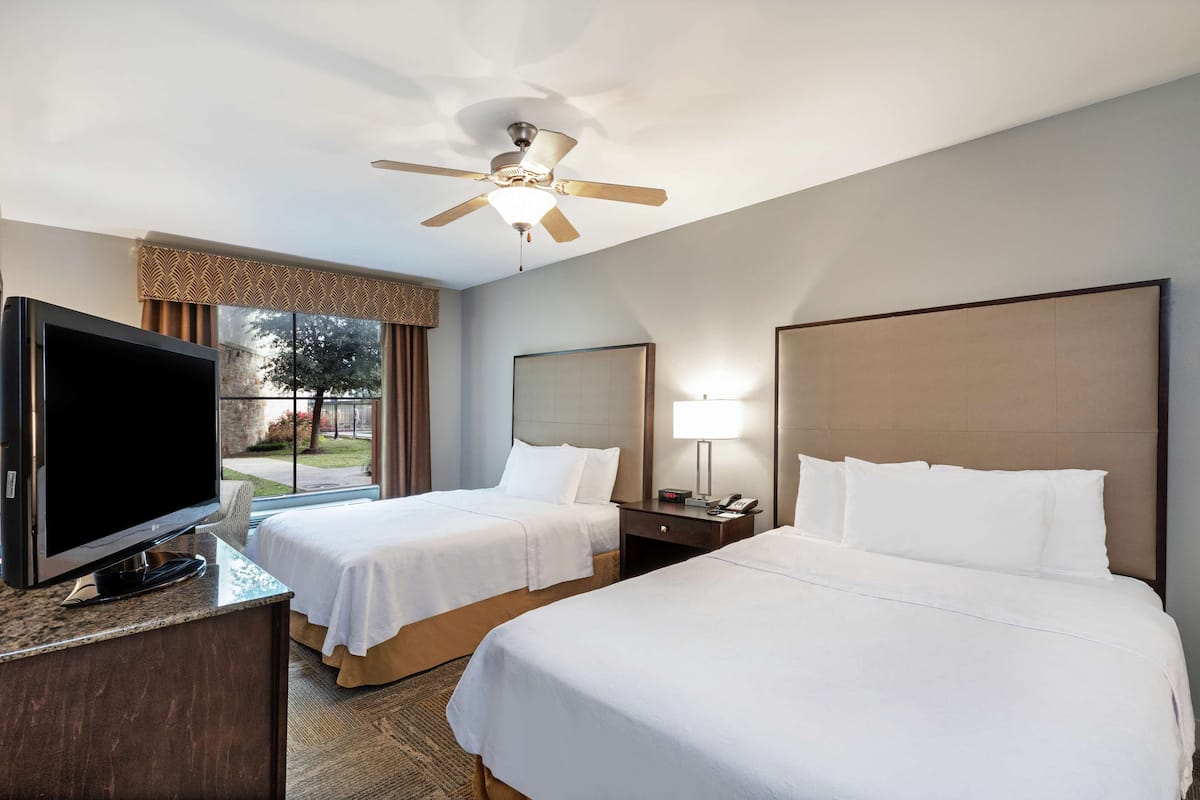 A hotel room with two beds, a TV, a ceiling fan, and a window with curtains.