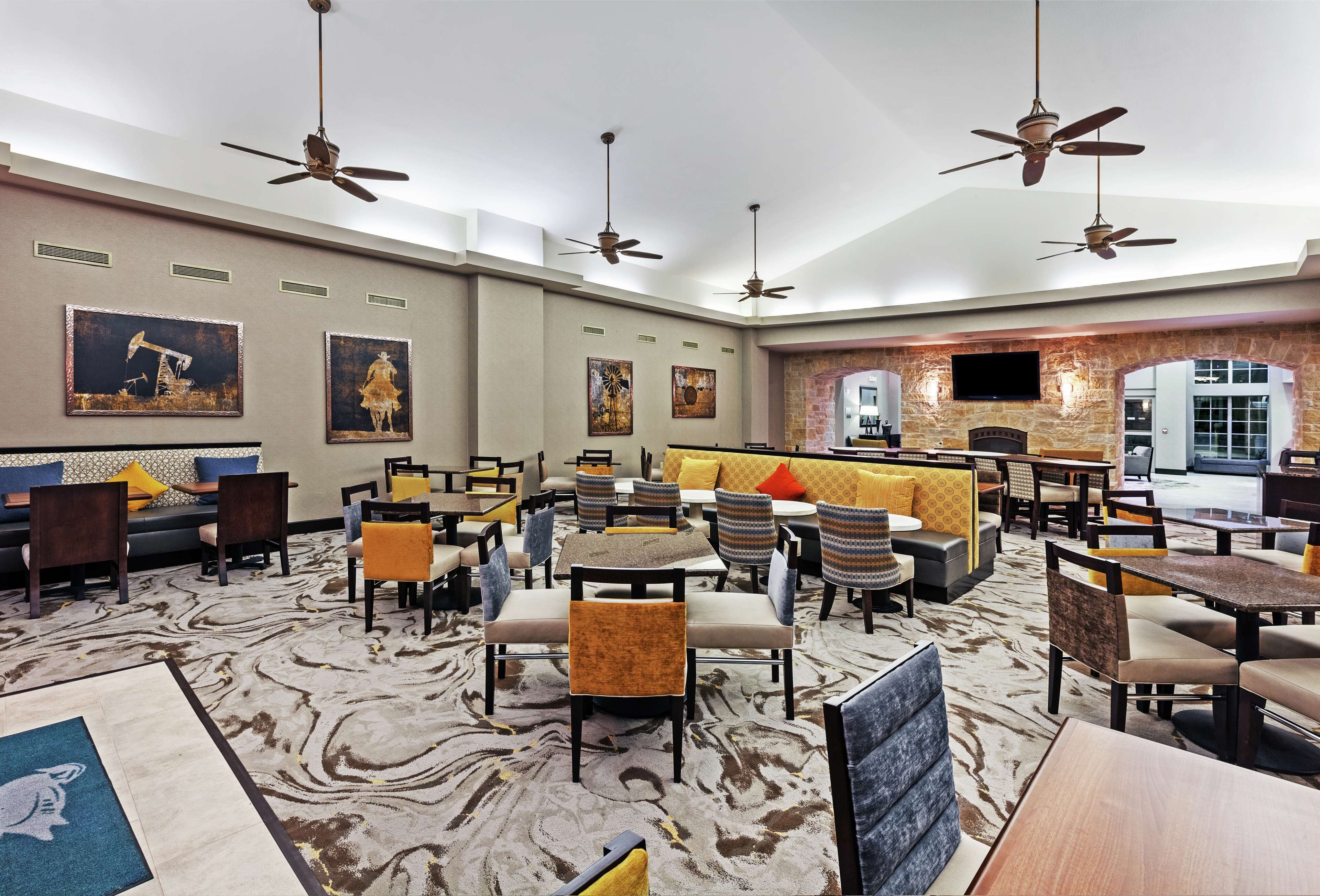 A hotel lobby with multiple seating areas, ceiling fans, artwork on the walls, and a stone archway leading to another room.