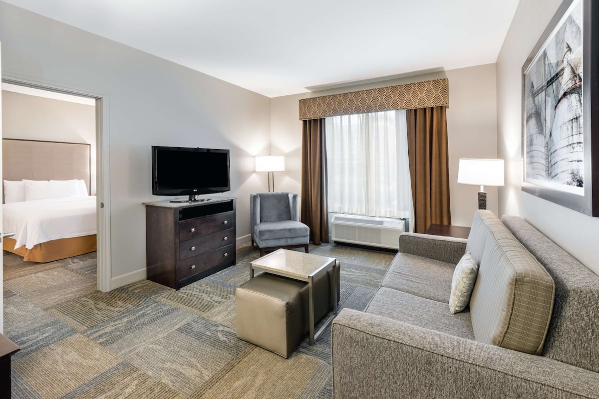 A hotel room with a bed, a television, a sofa, a chair, a coffee table, and a window with curtains.