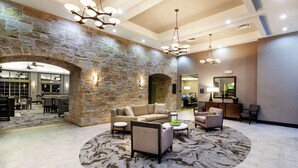 A spacious lobby with a stone wall, a round seating area, and a modern chandelier. - Homewood Suites by Hilton Waco (Waco)