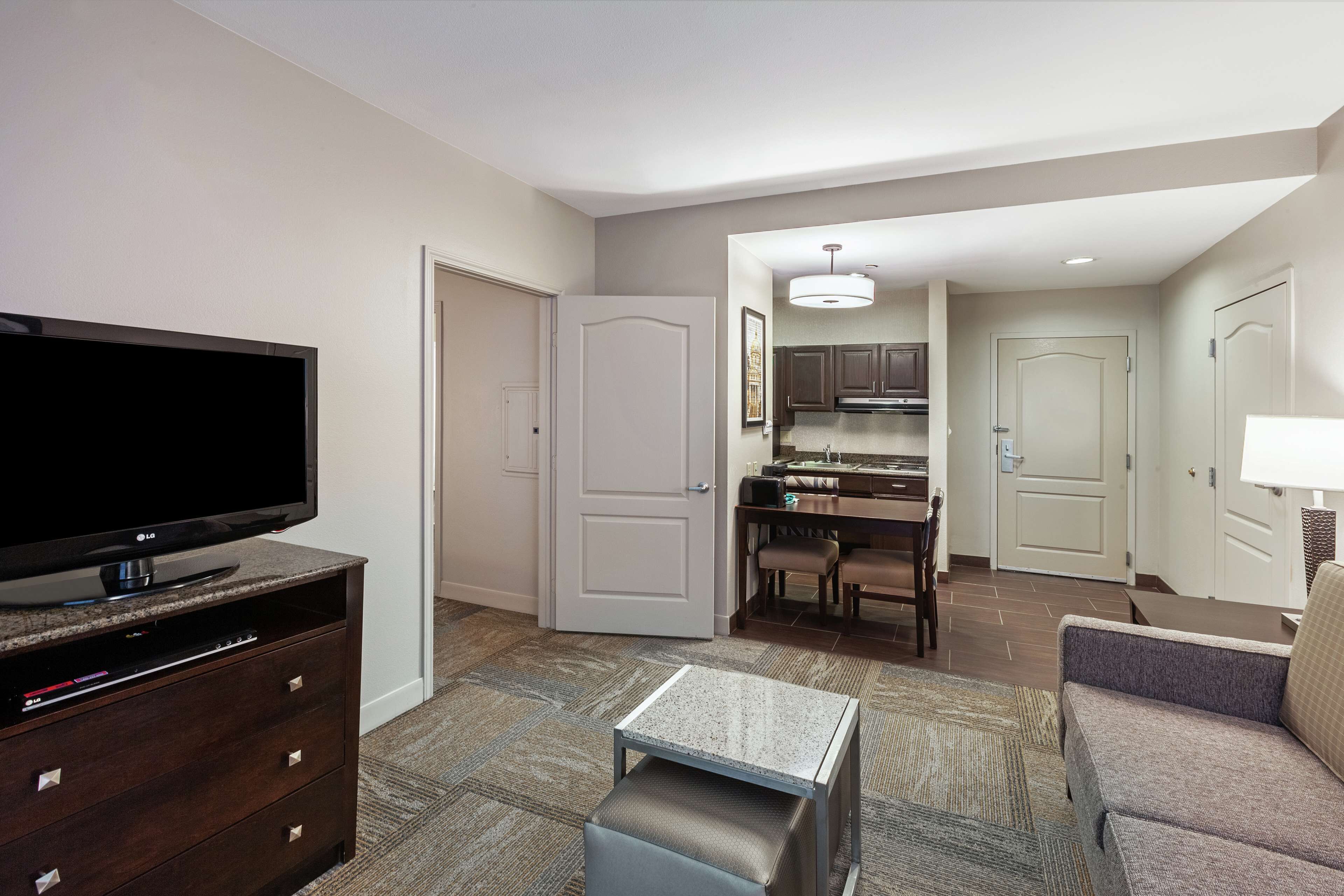 A modern living room with a flat-screen TV, a coffee table, a sofa, and a dining area with a table and chairs.