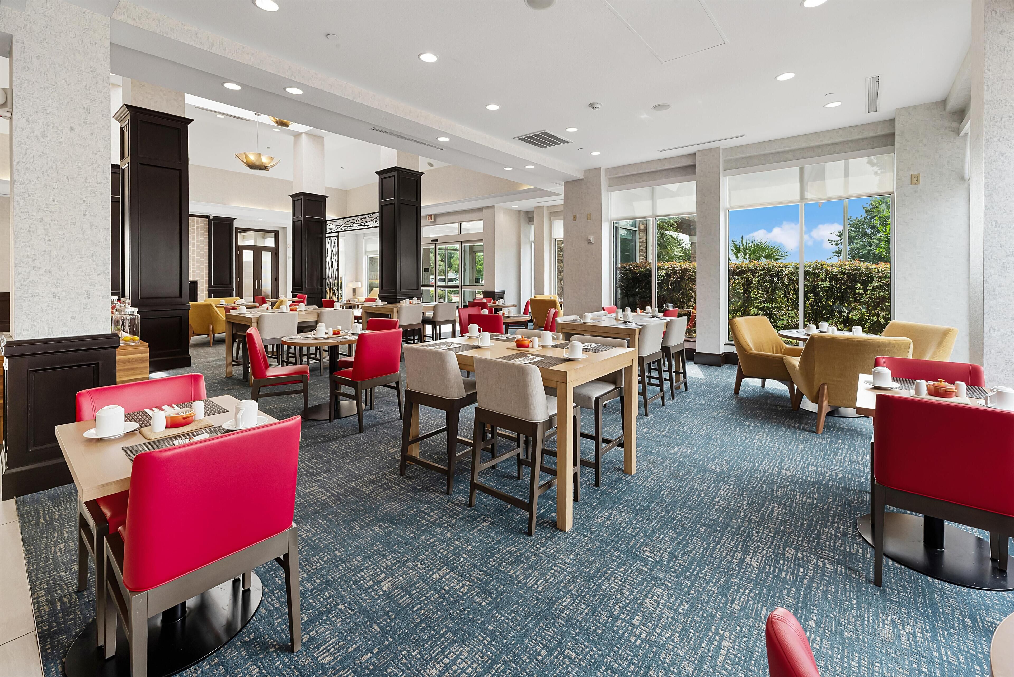 Un comedor amplio con varias mesas y sillas, ventanas grandes que ofrecen vistas al exterior, y un diseño de interiores moderno.