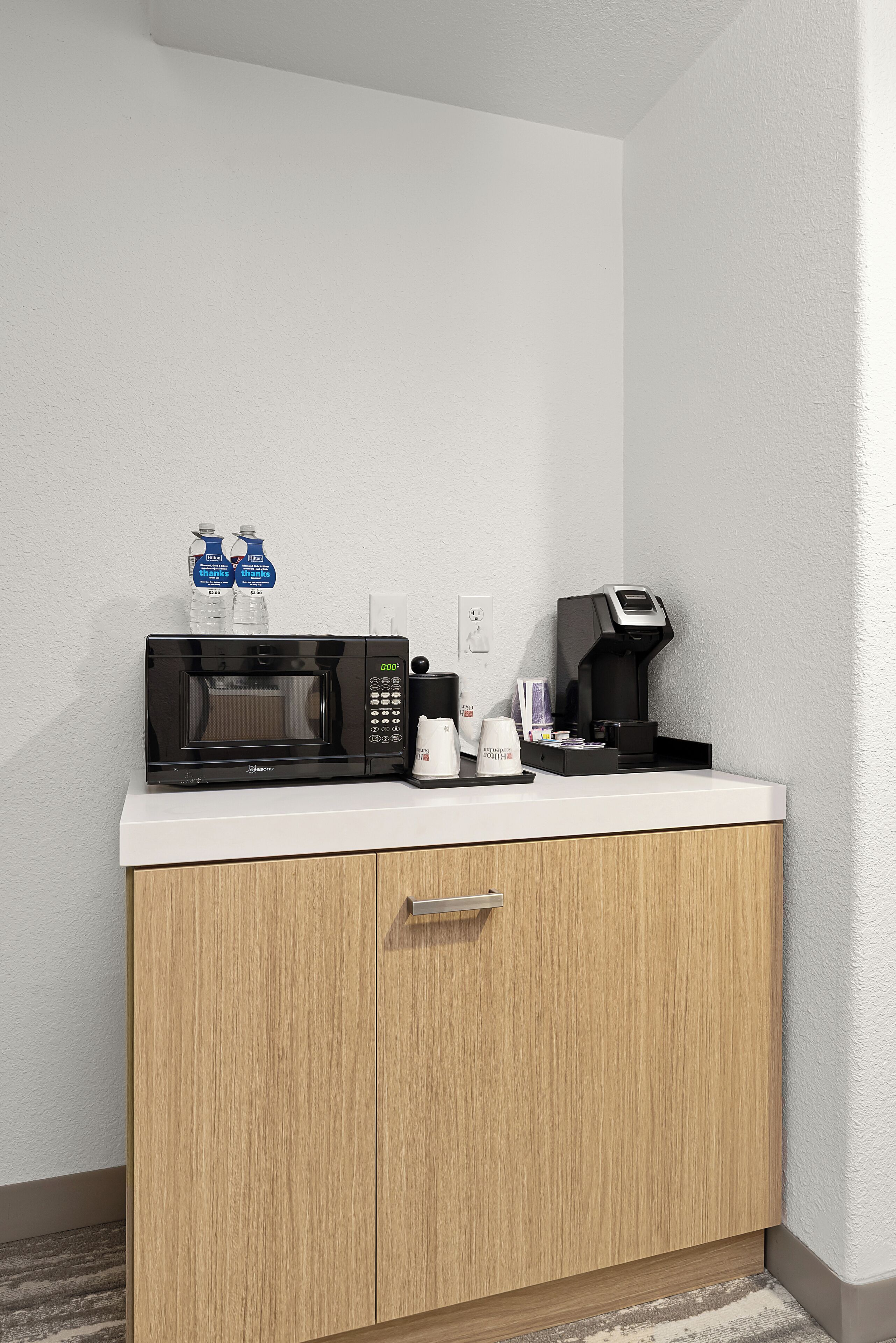 A kitchenette with a microwave, coffee maker, and water bottles.