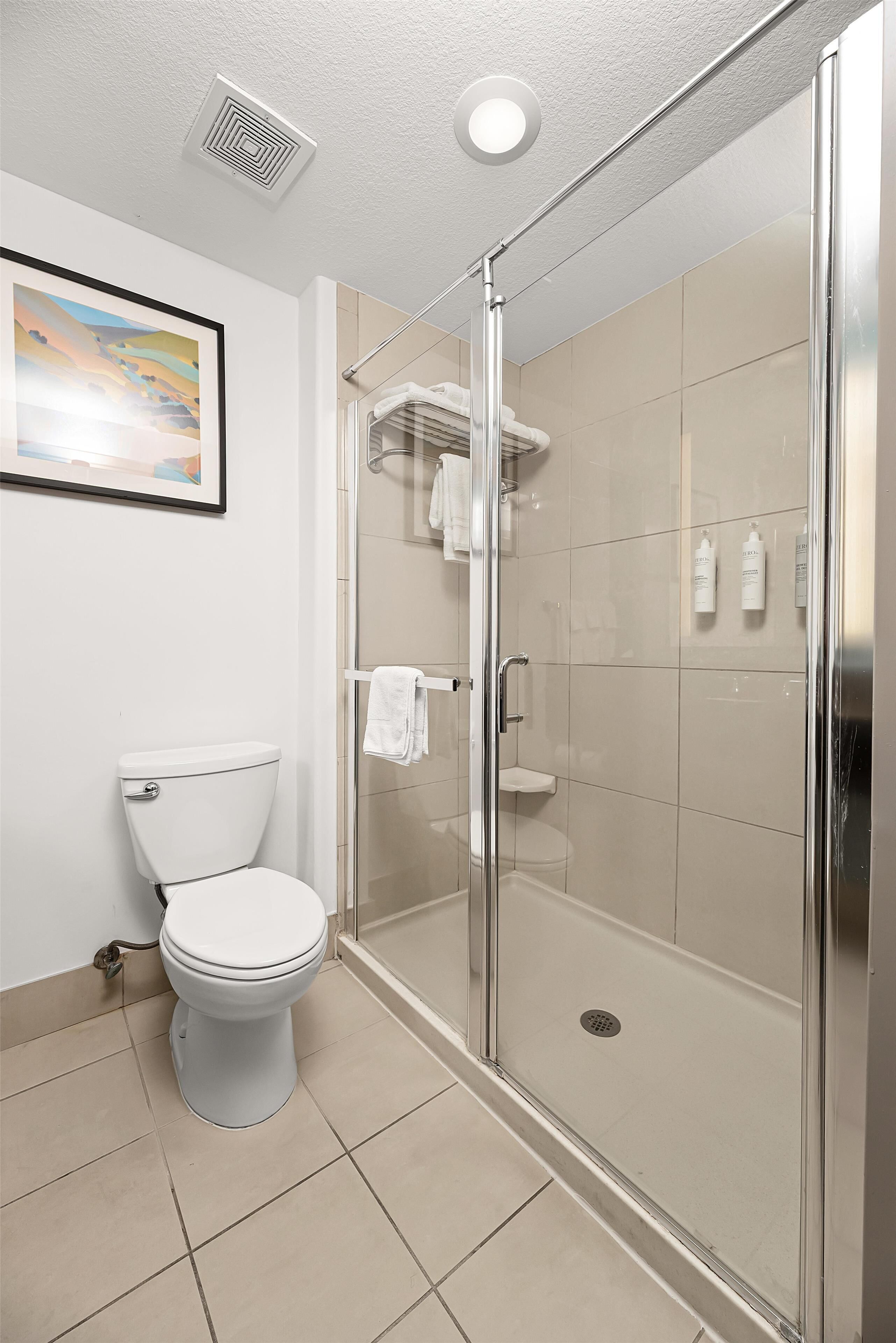 Un baño moderno con inodoro, ducha con mampara de vidrio y un cuadro enmarcado en la pared.