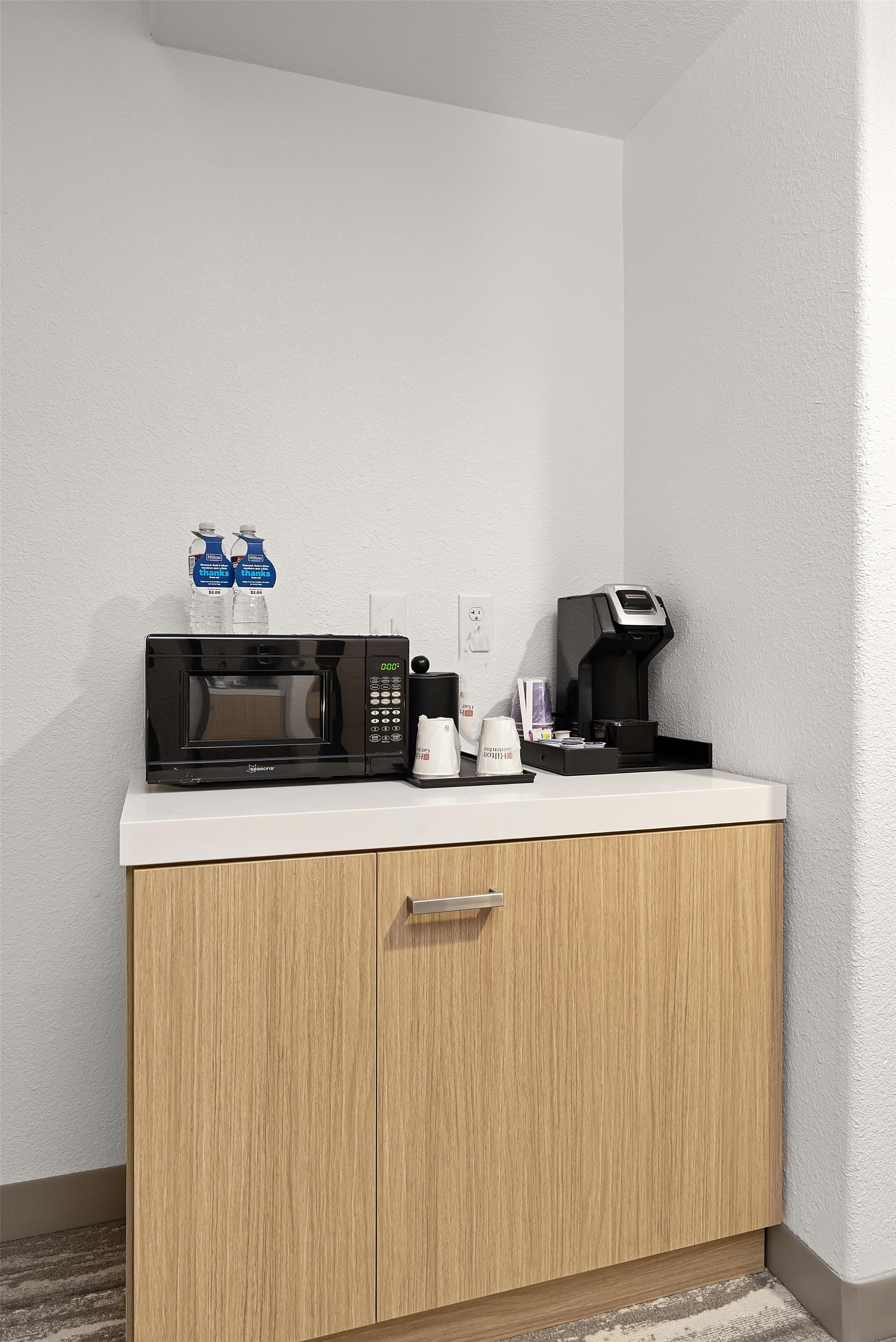 A kitchenette with a microwave, coffee maker, and water bottles.
