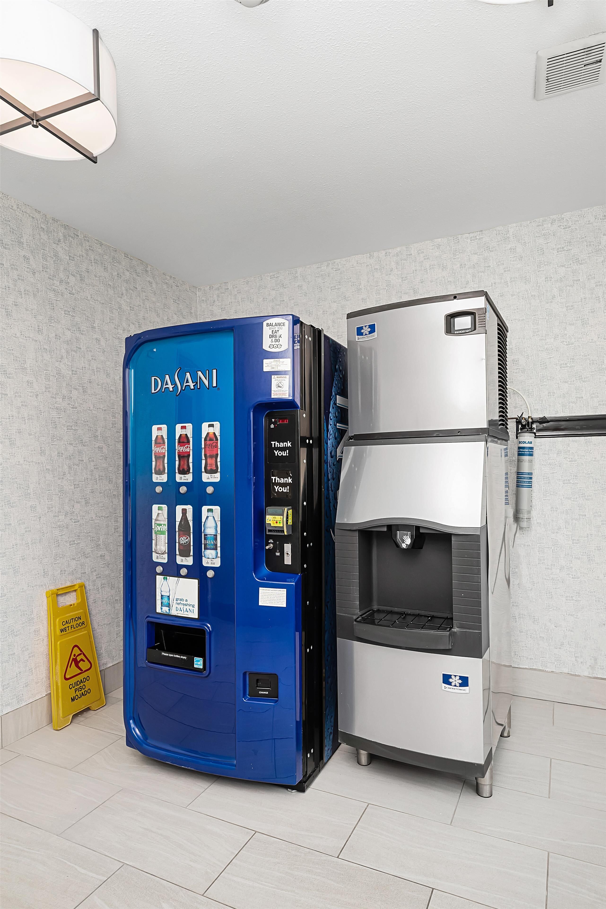 A beverage vending machine and a water dispenser in a room with tiled flooring and a caution sign.